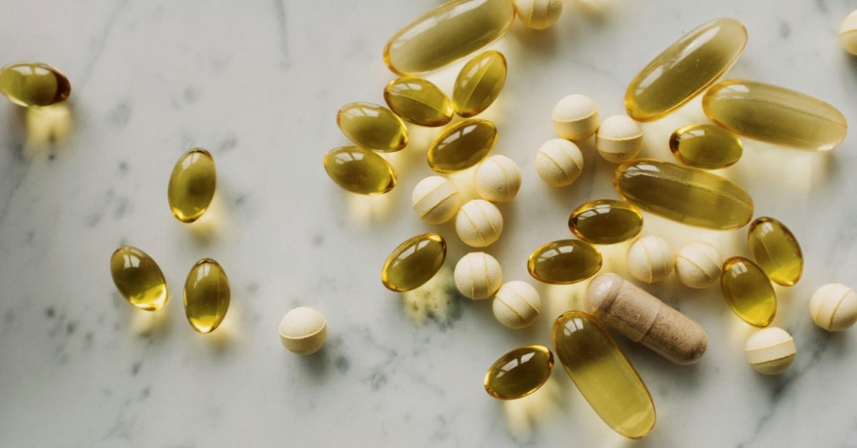 Simple supplement bottles of vitamin D, magnesium and fish oil on a kitchen counter next to whole food ingredients
