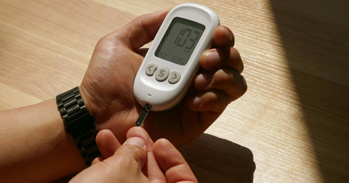 Man over 40 checking a blood glucose monitor while preparing a healthy high-protein meal