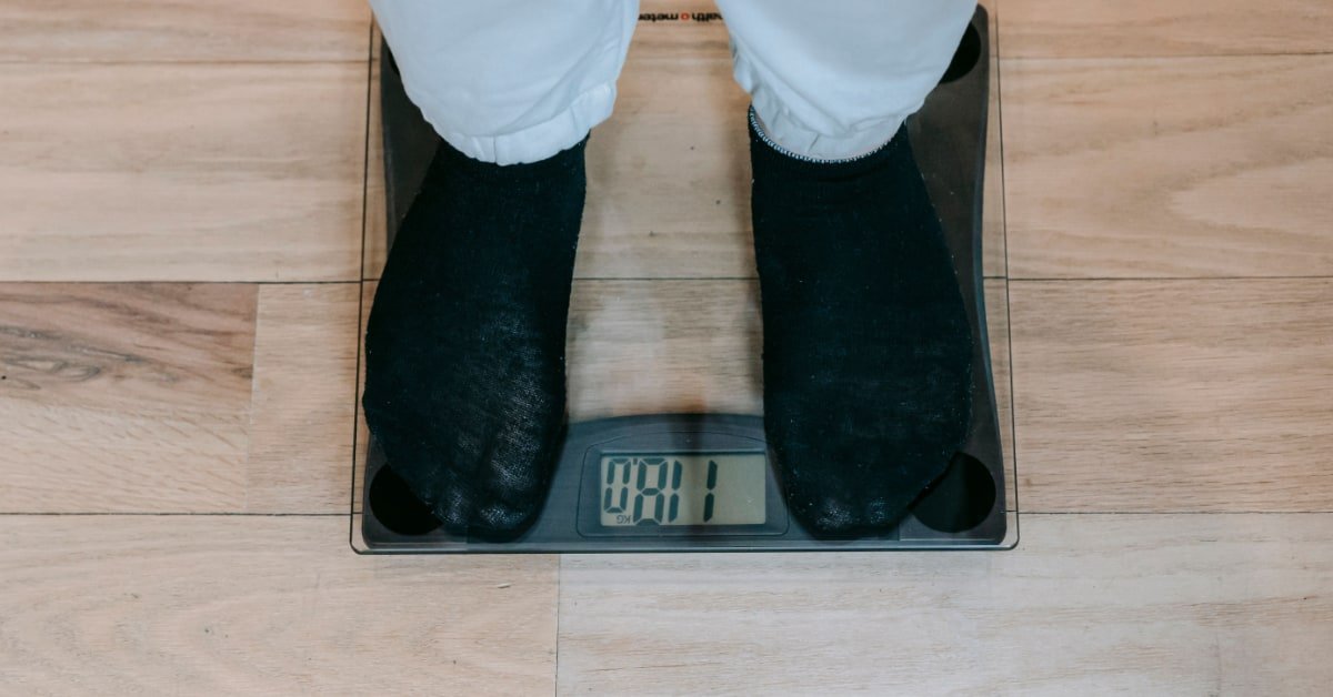 Man in his 40s looking at a weighing scale with a measuring tape nearby, home setting